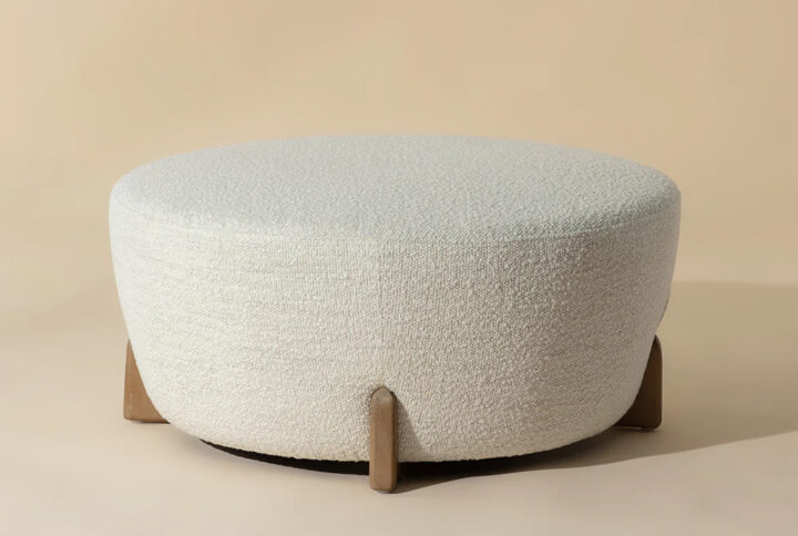 A white ottoman with wooden legs positioned against a soft beige background, showcasing a modern and elegant design