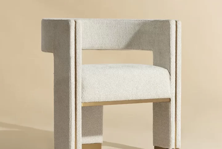 A modern chair featuring beige fabric upholstery and elegant gold legs, showcasing a stylish and contemporary design