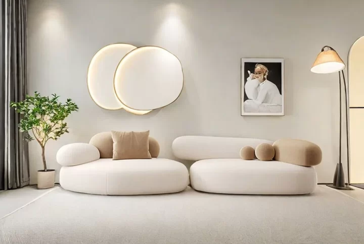 A bright living room featuring white furniture and a stylish round mirror on the wall, creating a modern aesthetic.