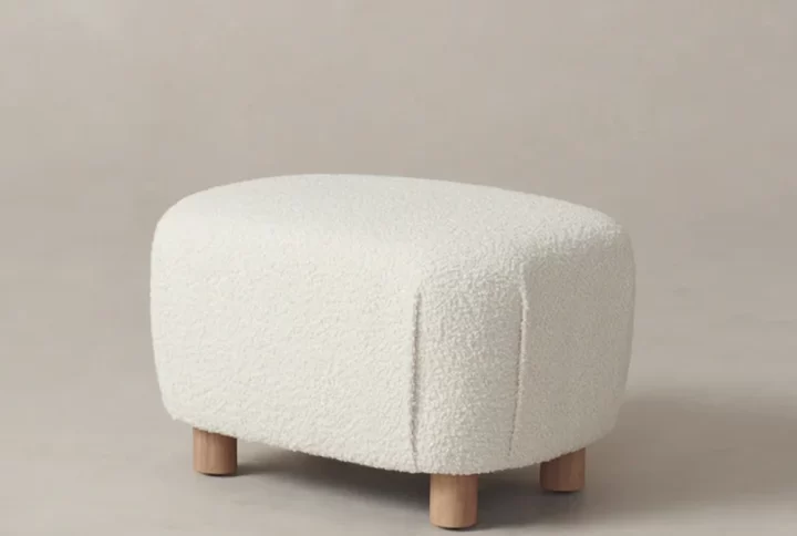 A white ottoman with wooden legs positioned against a clean white background, showcasing its elegant design