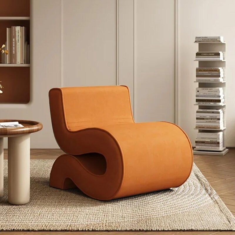 An orange Scandiline S-Chair in a cozy room filled with bookshelves, creating a warm reading atmosphere
