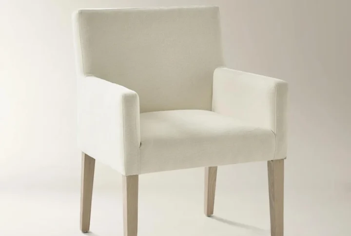Ivory upholstered armchair with boxy silhouette and light wood tapered legs in modern setting.