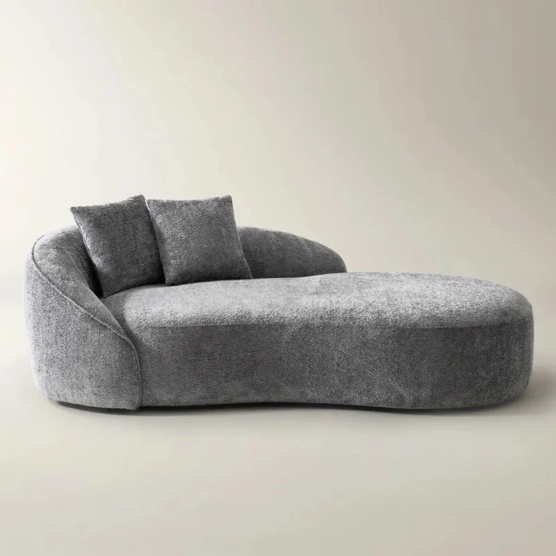 Light gray curved chaise lounge with plush chenille upholstery and matching throw pillows in a modern setting.