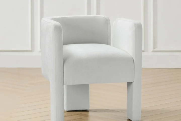 Modern white upholstered armchair with curved backrest and cylindrical legs in minimalist interior.