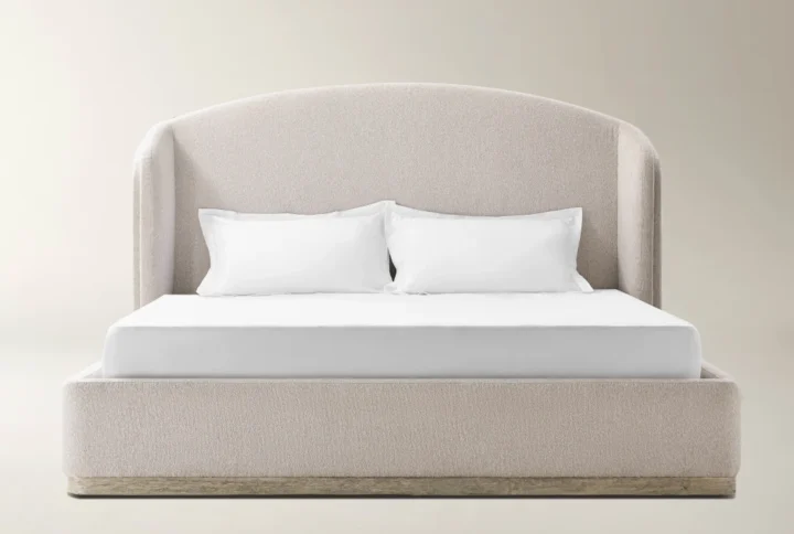 Light beige upholstered bed with curved headboard, wooden base accent, and minimalist styling.