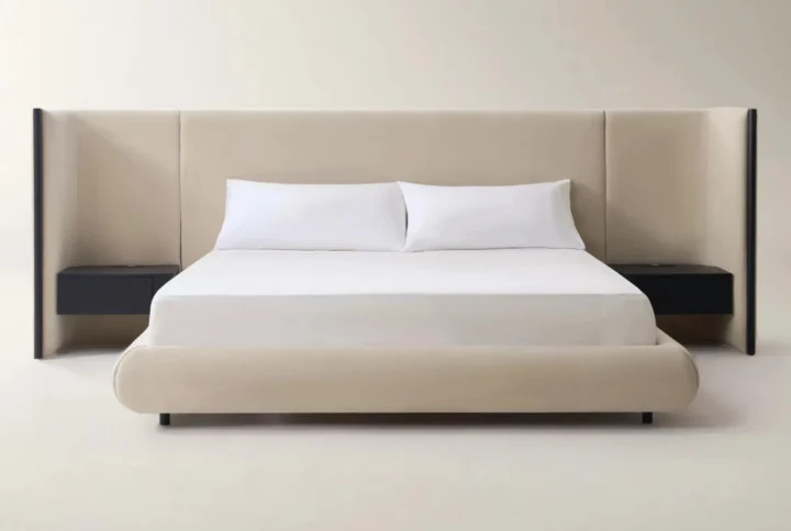Beige upholstered bed with extended headboard and built-in black nightstands in a minimalist bedroom.